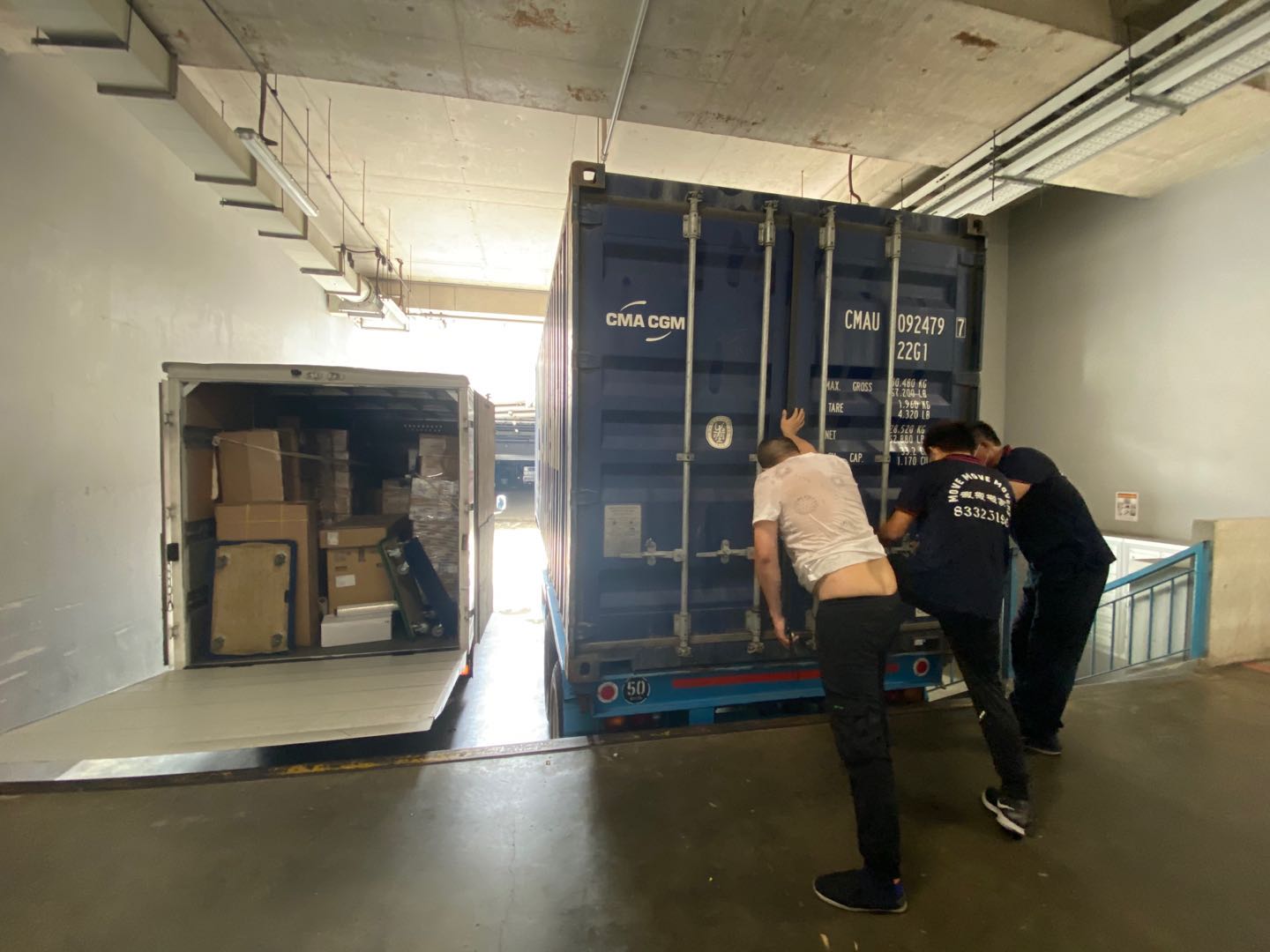 Container docking at loading bay - move move movers – move move movers – move move movers Crew positioning a shipping container beside a loaded box truck at a Singapore loading bay