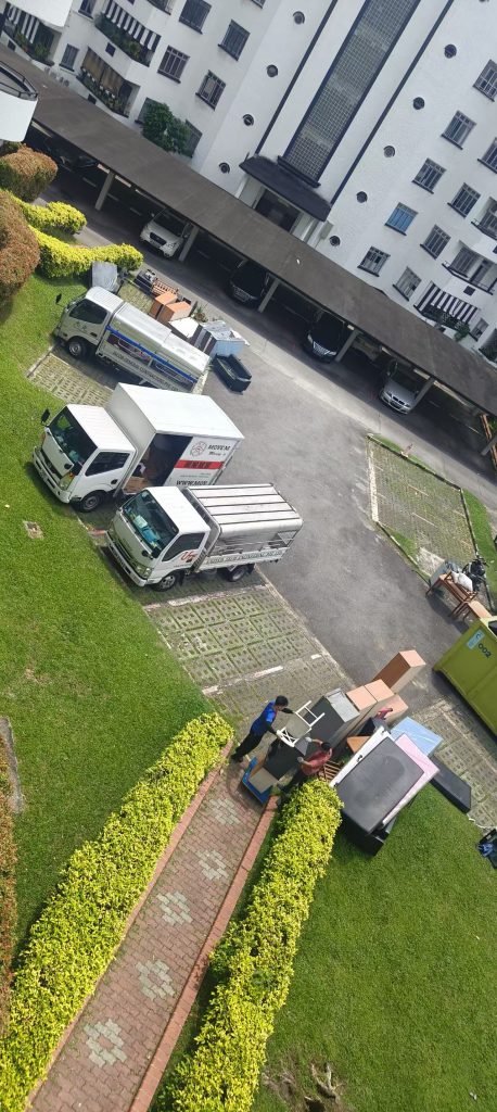 Workers moving bulky furniture toward a skip tank with service trucks nearby