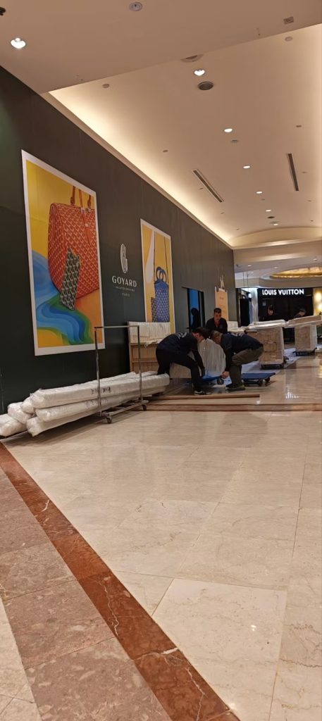 Crew adjusting dolly wheels and protective sheets before moving wrapped fixtures