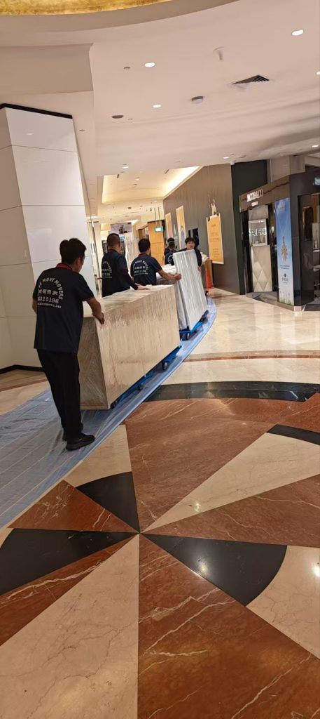 Crew moving long wrapped fixtures along an indoor mall corridor