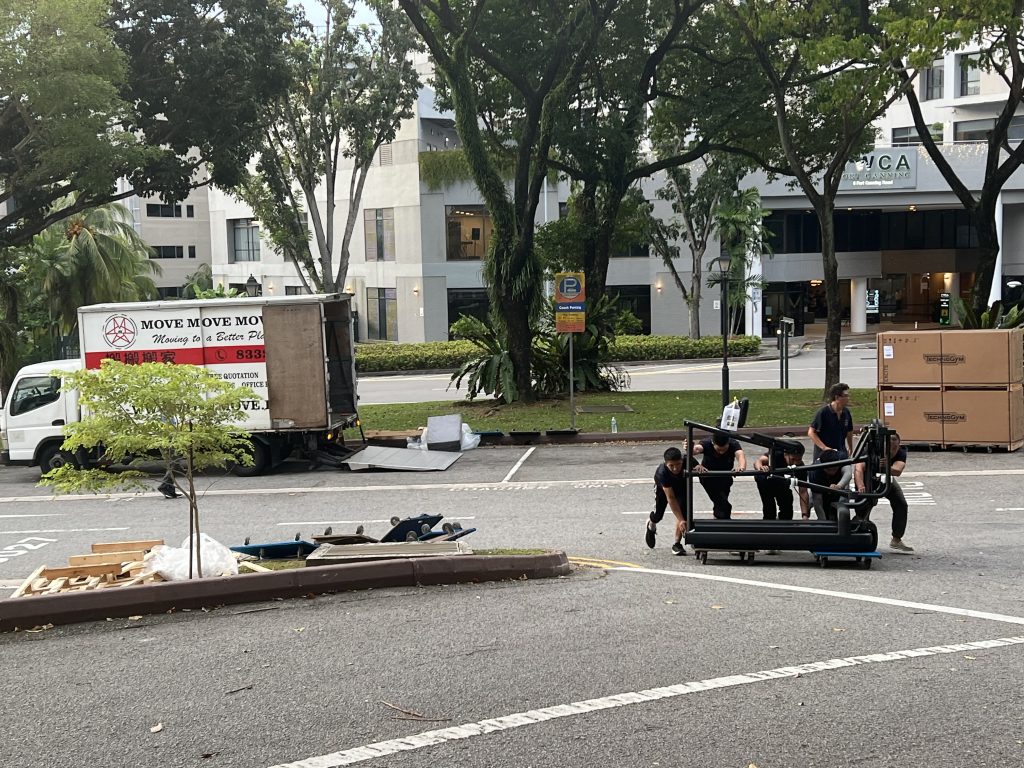 Crew pushing a treadmill frame on a dolly across an outdoor loading area