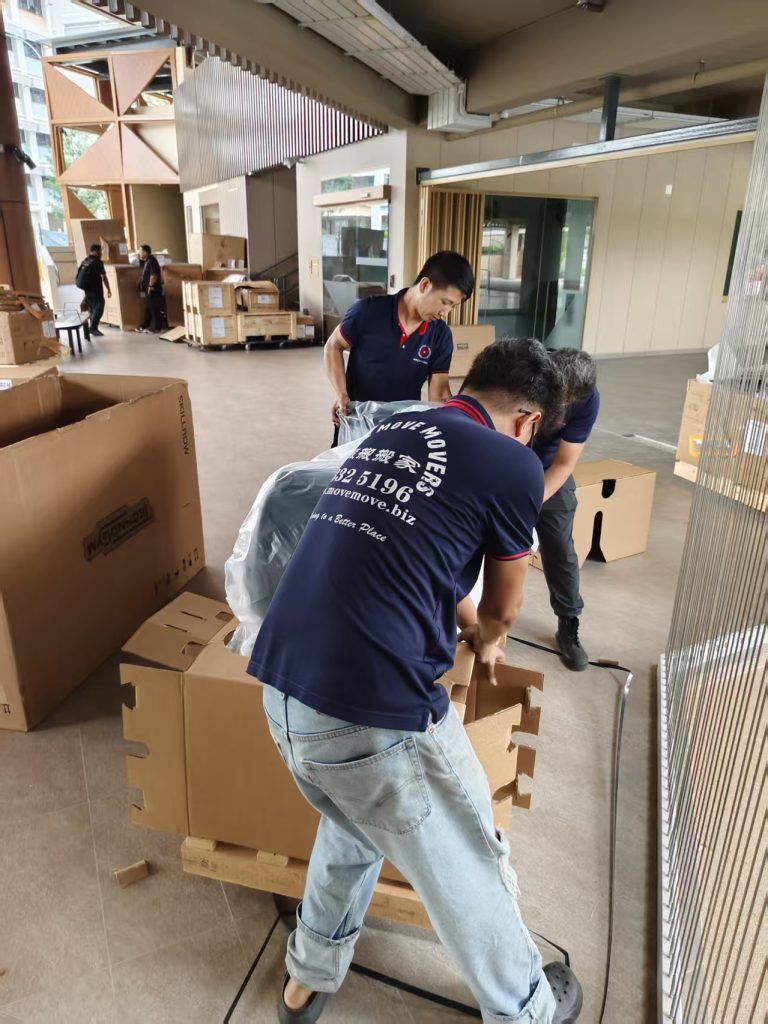 Three movers opening protective cartons around gym equipment in an indoor staging area