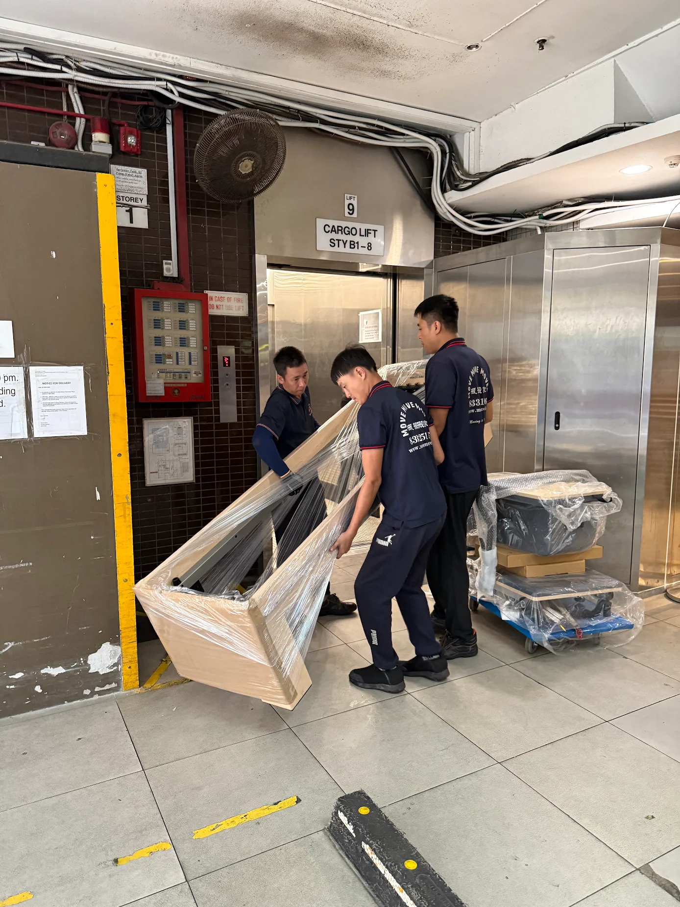 Wrapped sofa moving through a condo cargo-lift lobby in Singapore