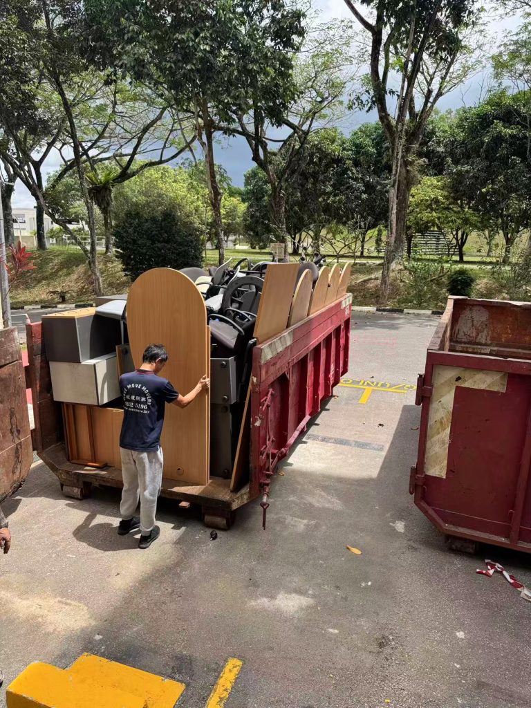 Worker guiding bulky furniture loaded into a red skip tank at an outdoor disposal site
